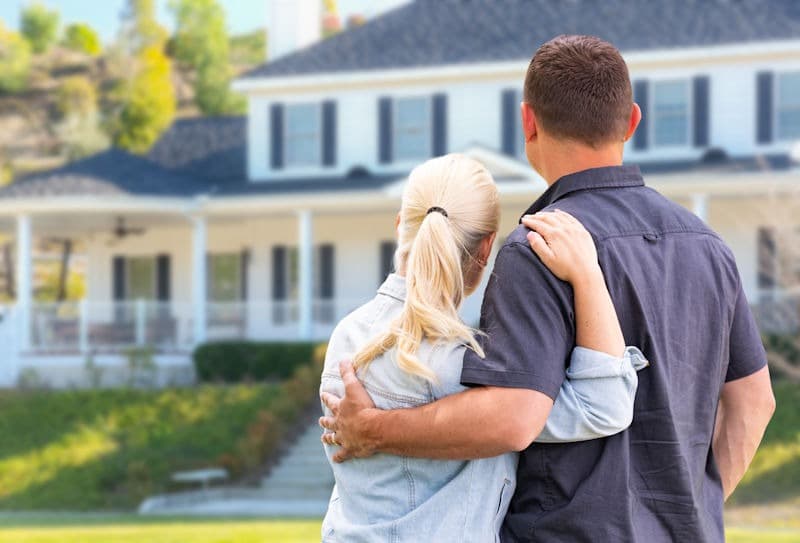 Young Adult Couple Facing Front of Beautiful House.