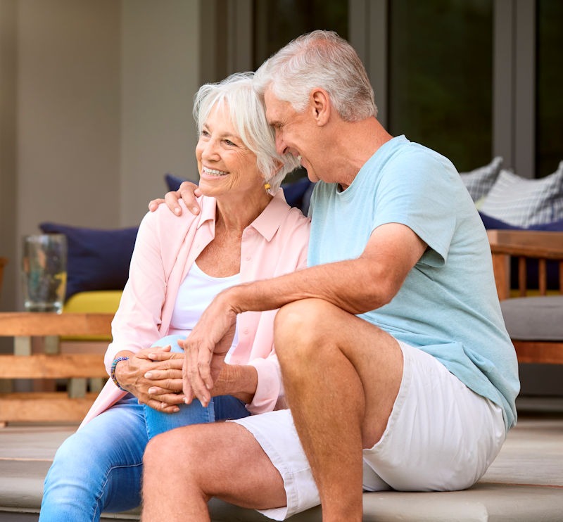 Loving Senior Couple Sitting Outdoors On Deck At Home Together